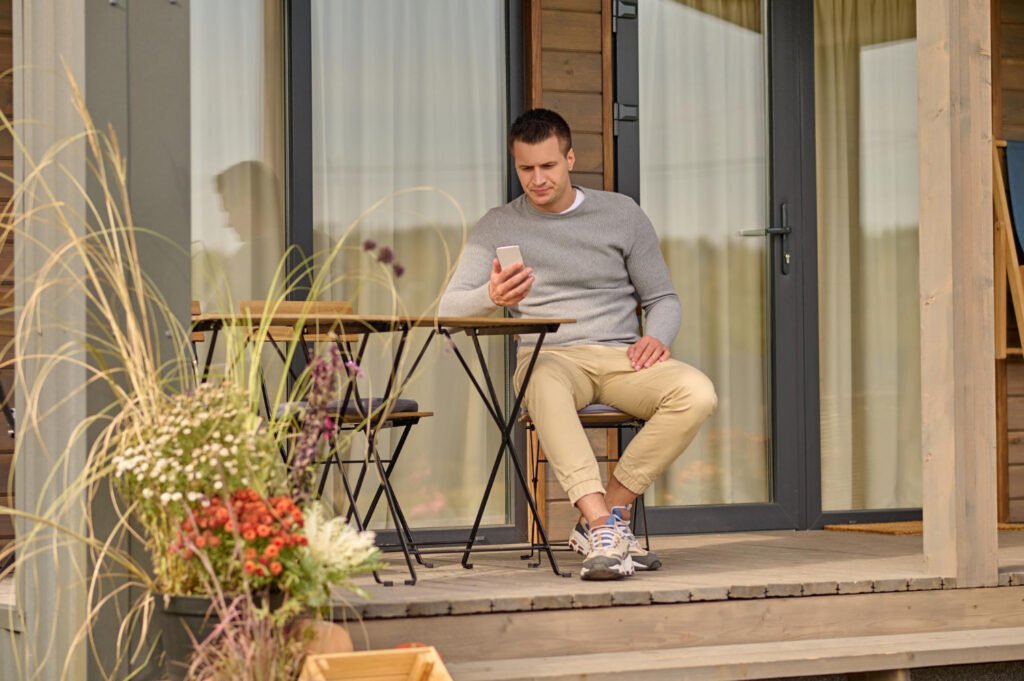 man sitting table near house looking smartphone
